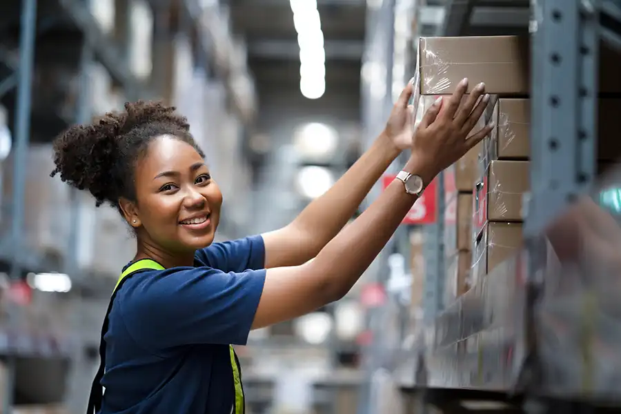 smiling worker putting boxes on a warehouse shelf